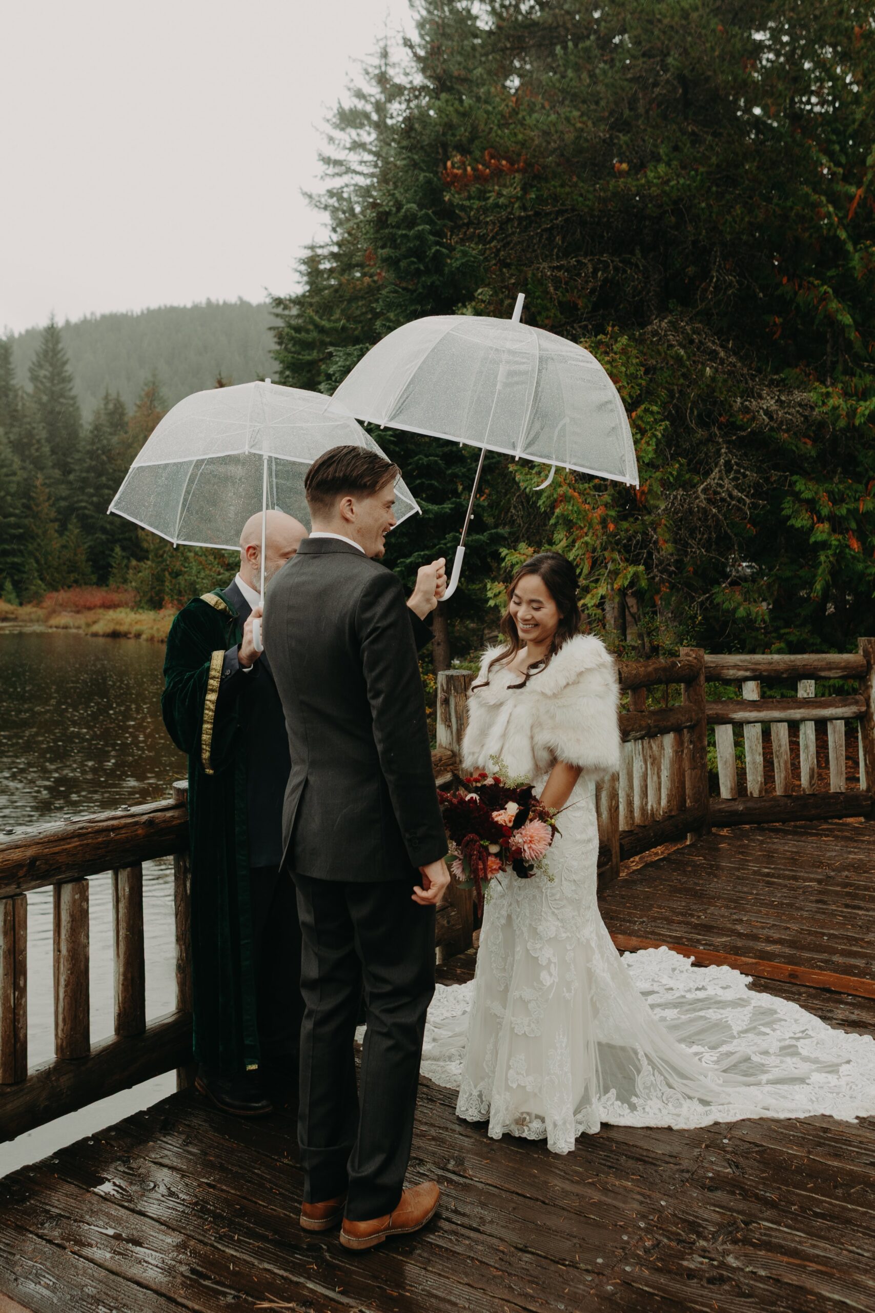 bride happily looks down as her groom holds an umbrella over her as they exchange vows at trillium lake