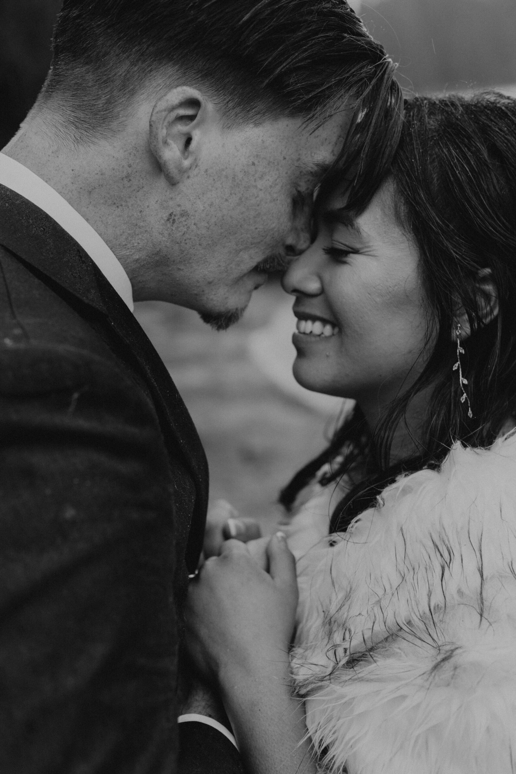 black and white photo of a groom pressing his forehead to his bride's as she smiles