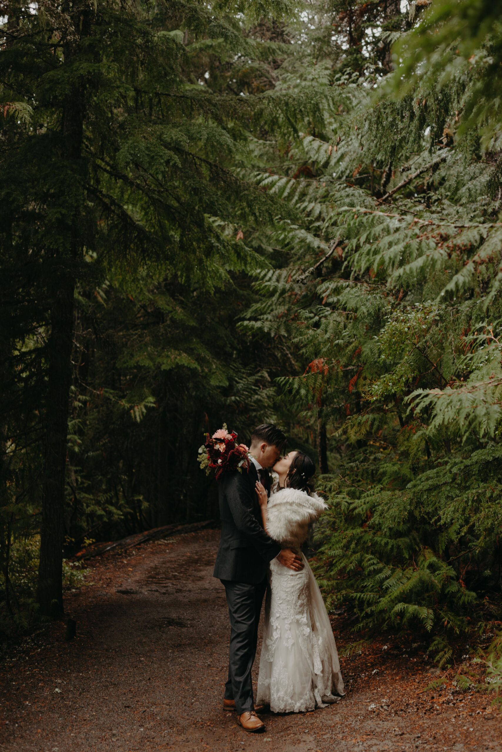 bride and groom embrace and kiss on a forested trail at mount hood