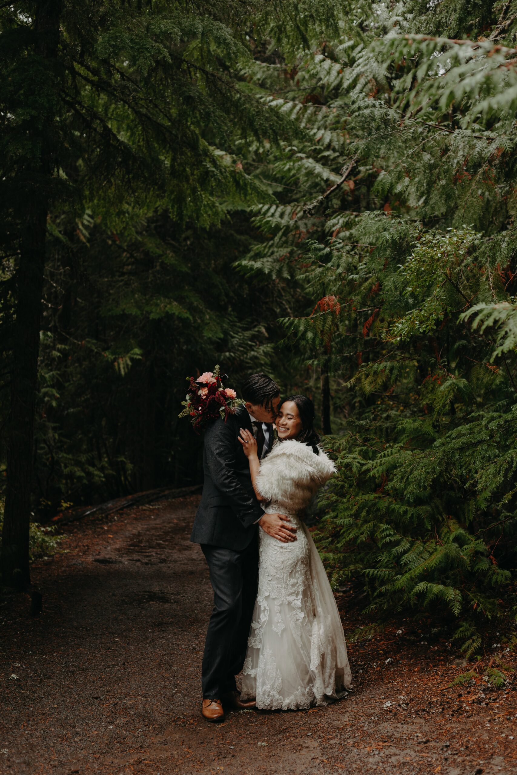 bride and groom embrace on a moody forested trail 
