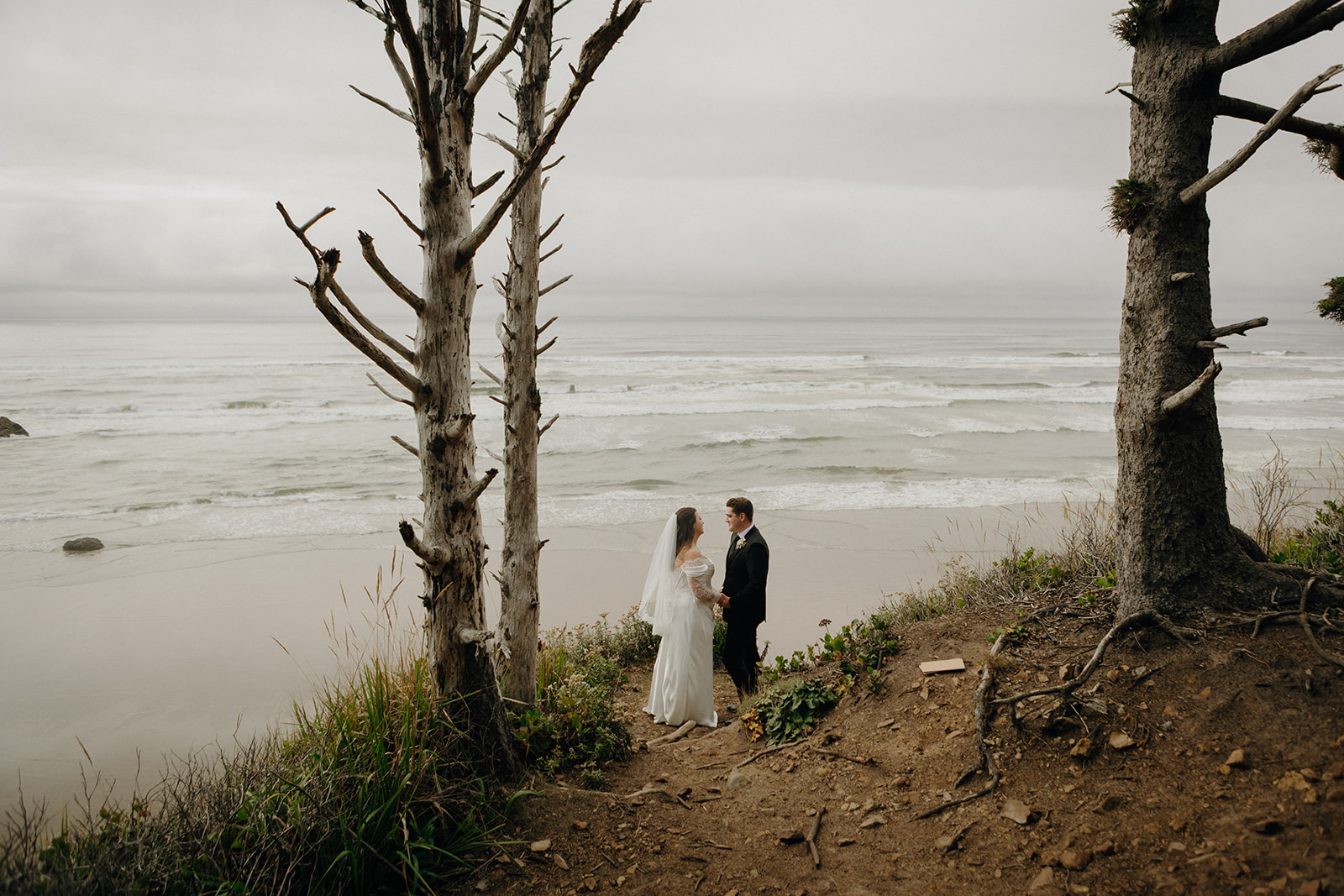 Bride and groom kiss passionately on a cliffside, surrounded by lush greenery and rocky formations. The scene conveys romance and natural beauty.