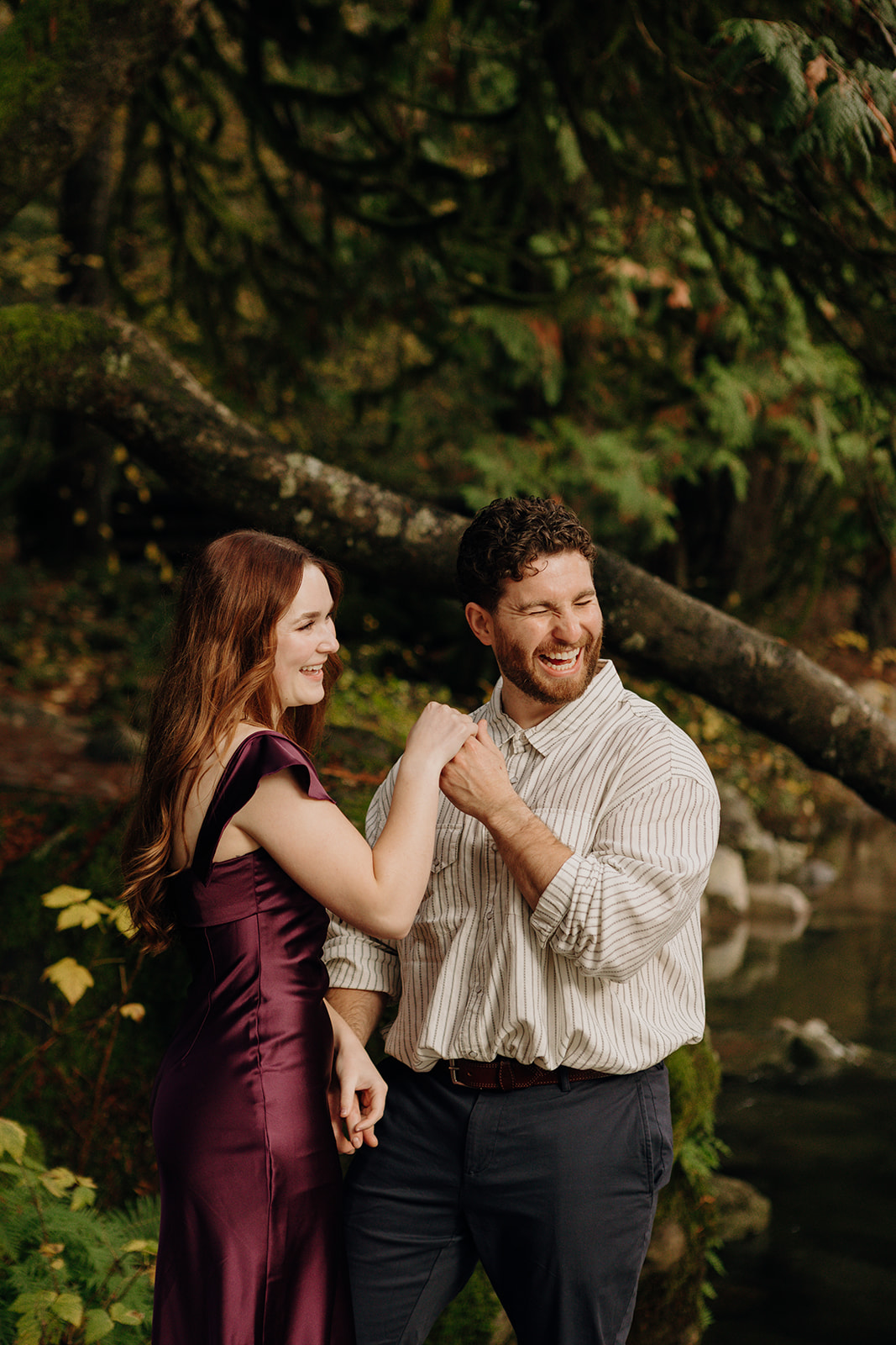 a man holds a woman's hand as she smiles at him and he cracks a large smile closing his eyes