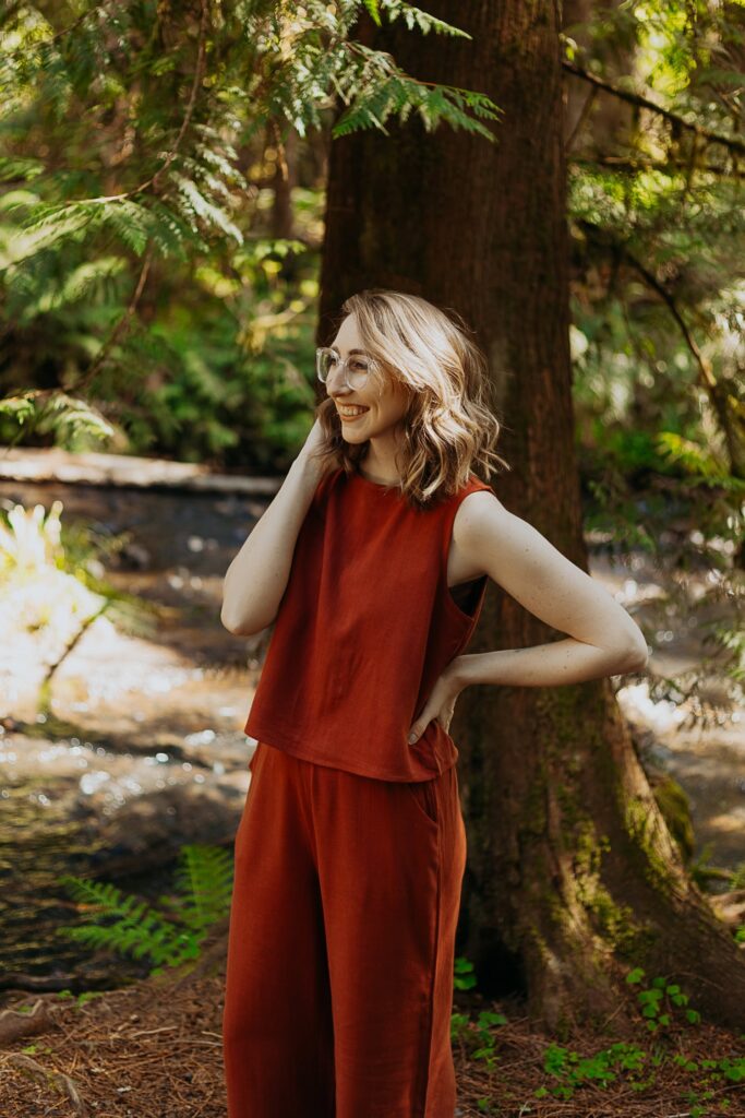 a woman in a burnt orange two piece set stands in a forest smiling and looking away from the camera