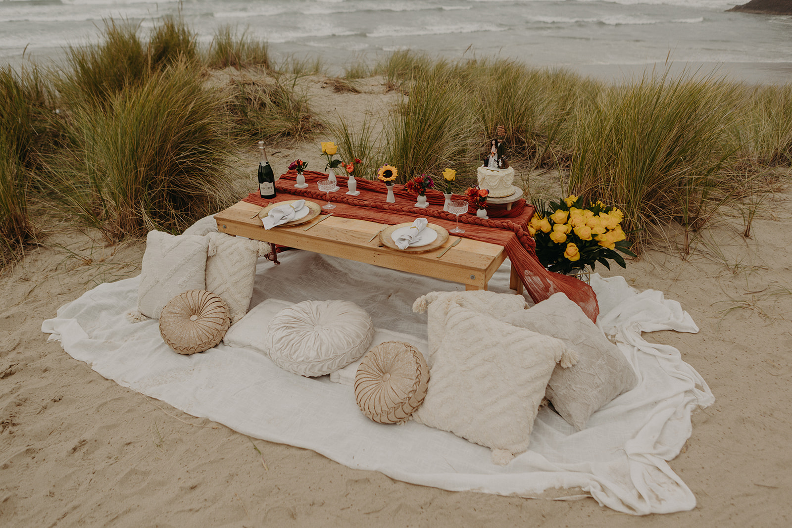 luxury picnic on cannon beach with pillows and table set up and orange table runner