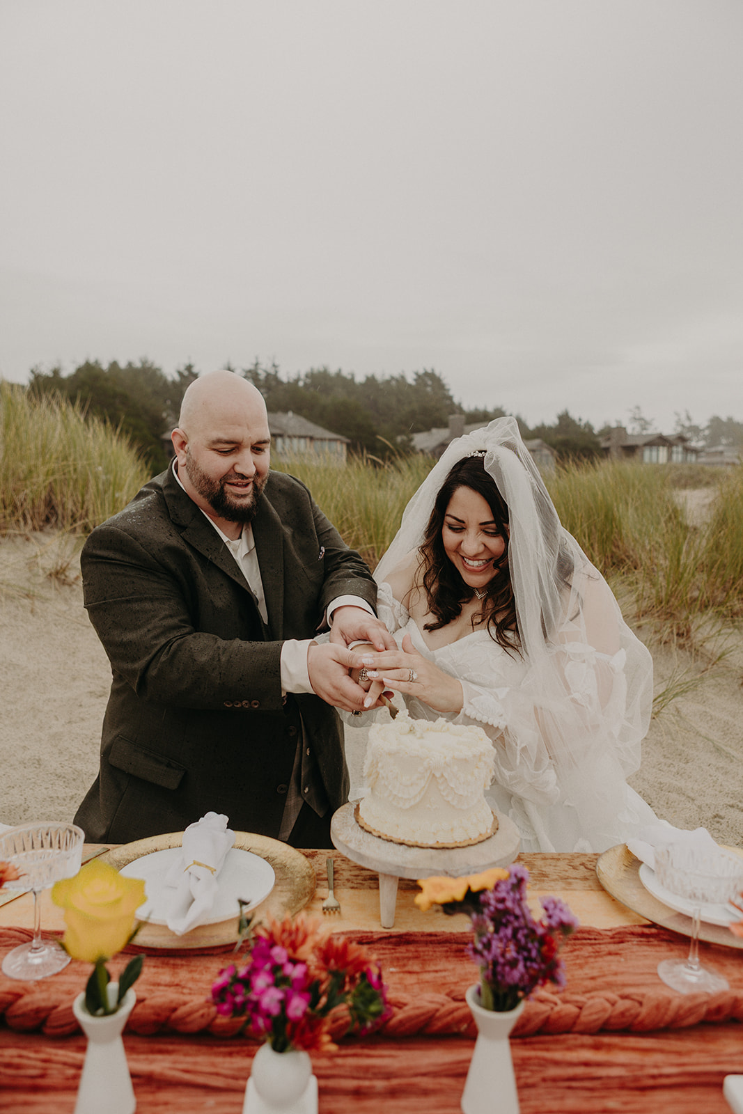bride and groom cut the cake on a beach with an orange table runner in the foreground