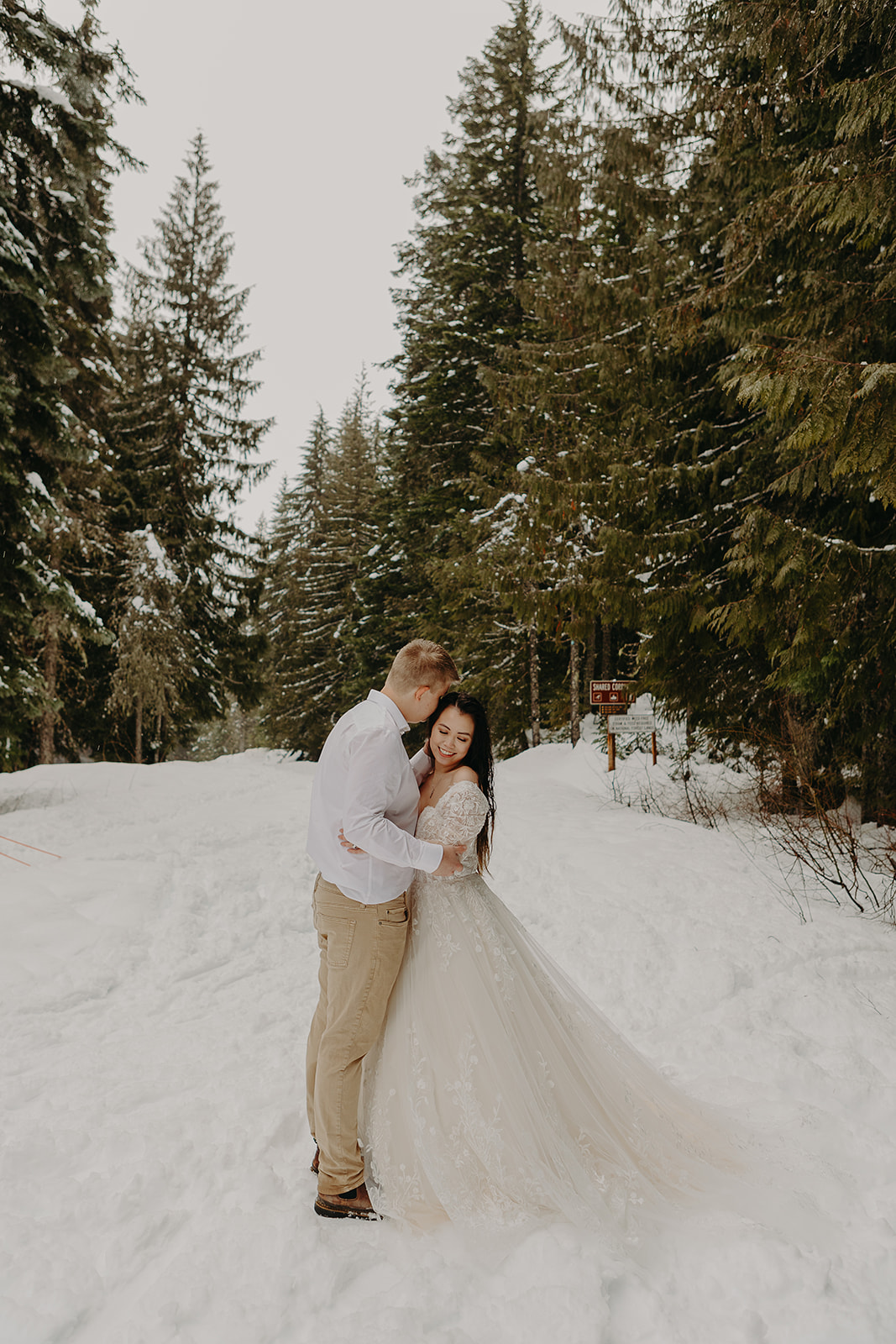 man and woman embrace in the middle of a wintery trail as snow falls at Mount Hood