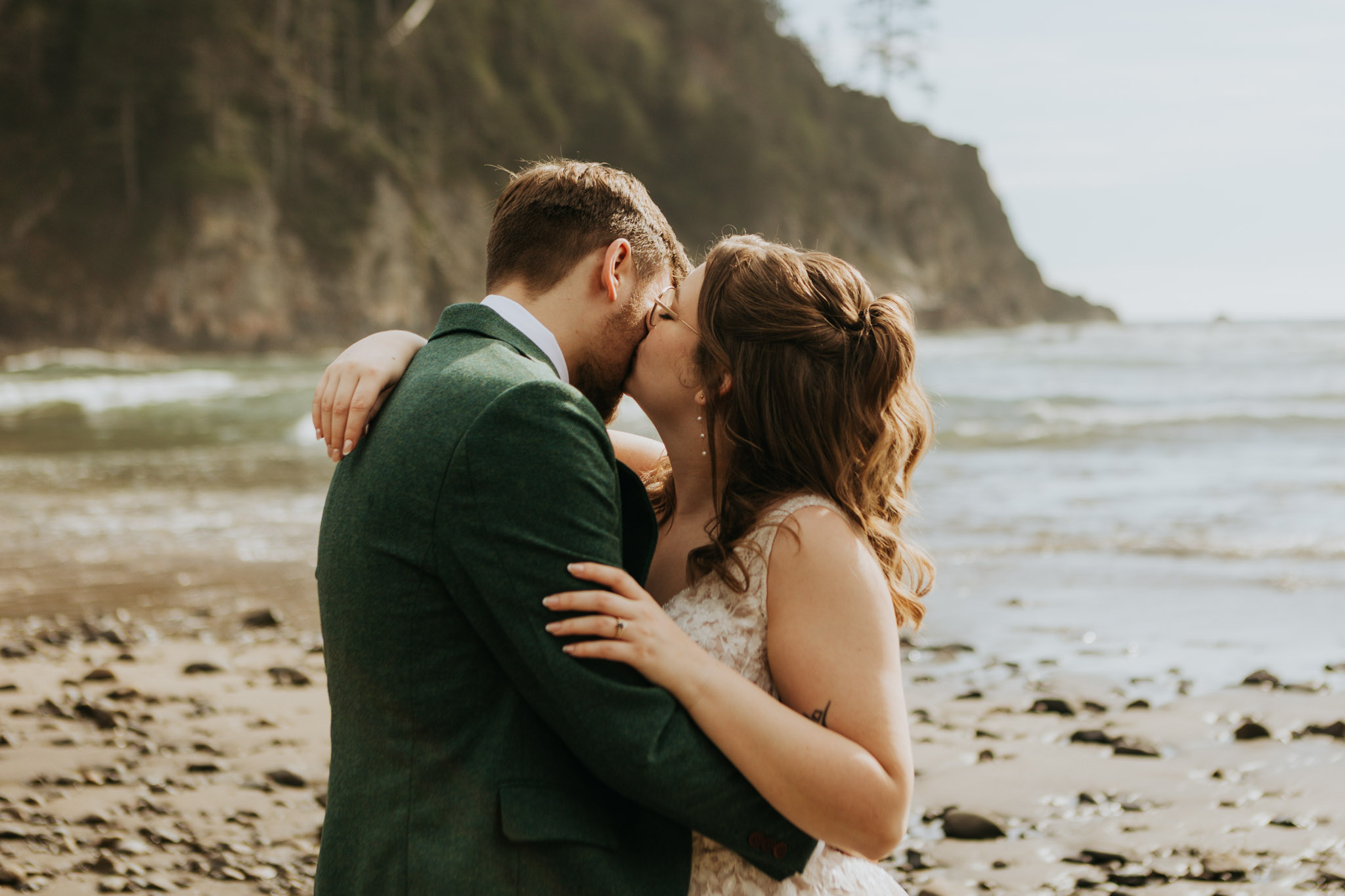 A couple shares a romantic kiss on a rocky beach, with waves and cliffs in the background. The scene conveys love and tranquility.
